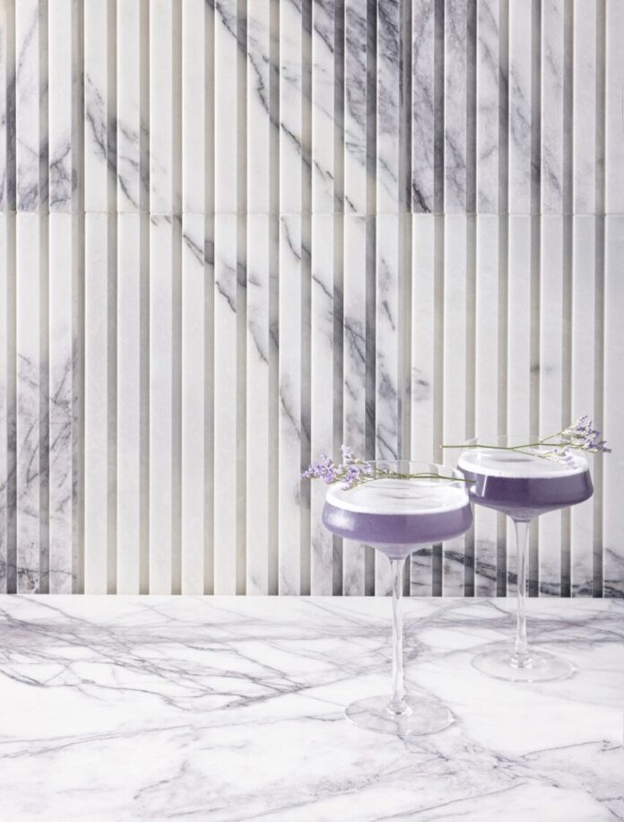 Two tall glasses hold surrealism purple cocktails against a lavender and white wallpaper.