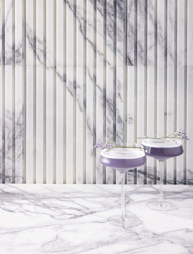Two tall glasses hold surrealism purple cocktails against a lavender and white wallpaper.