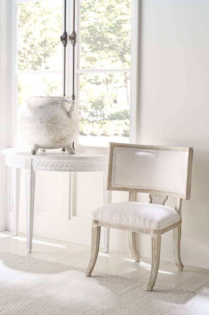 A white chair with warm gold trim and a white tables with a white marble statue on top from Antiquarian in Pittsburgh.