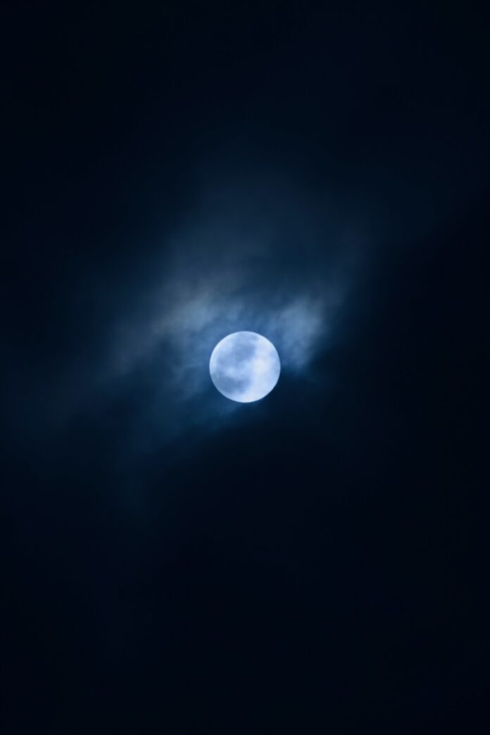 A moon lights up a small part of a June night sky with clouds overhead.