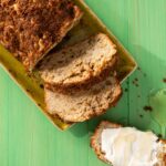 A loaf of coffee cake with rhubarb, apple, and walnut lays sliced on a green picnic table.