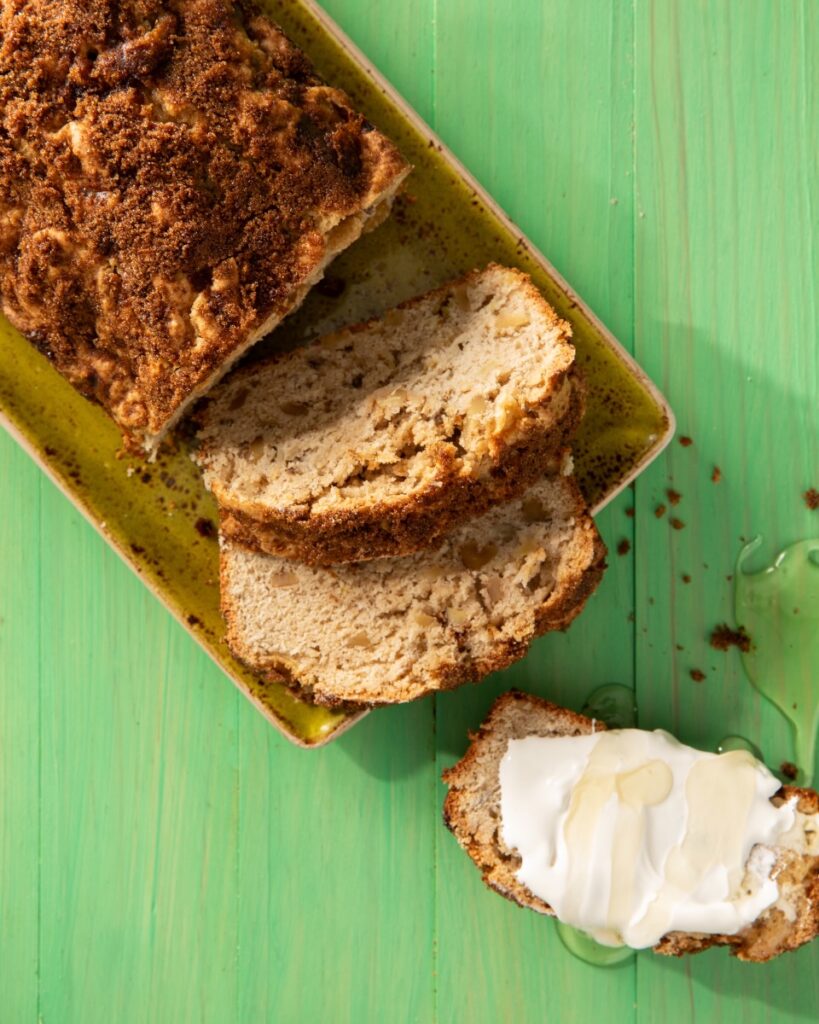 A loaf of coffee cake with rhubarb, apple, and walnut lays sliced on a green picnic table.