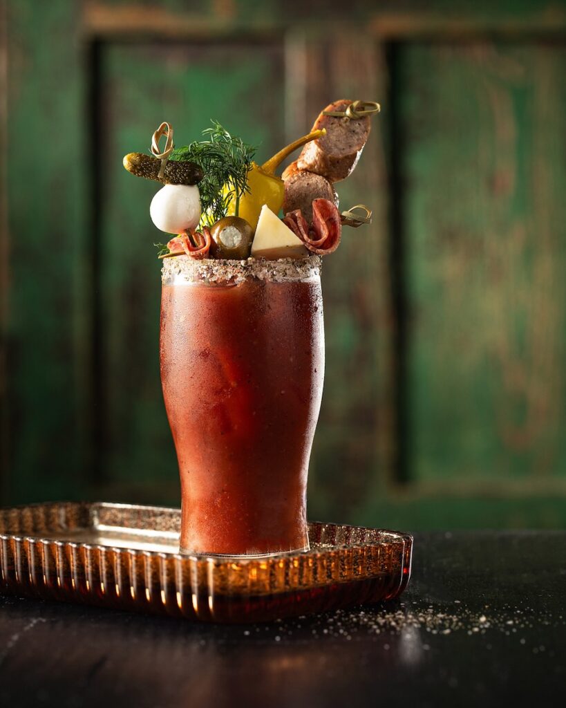 An antipasto virgin non-alcoholic bloody mary with various antipasto garnishes like cocktail onions, olives, cheese slices, and salami.