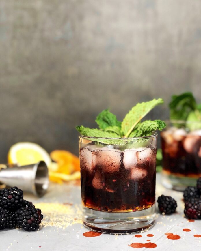 A glass with a Blackberry Gin Shrub featuring ice and a mint leaf garnish.