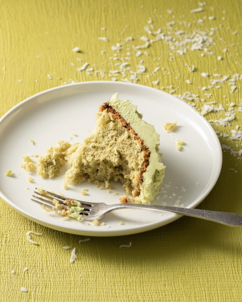 A half eaten piece of coconut matcha chiffon cake on a white plate with a fork on it.