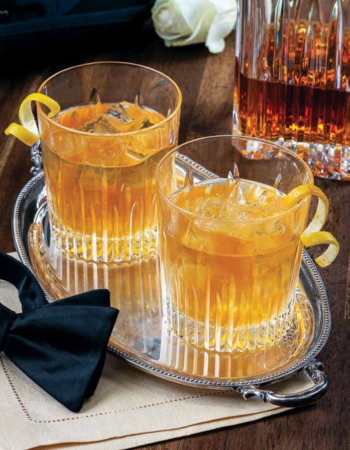 Two glasses of Fish House Punch with lemon twist garnishes sit on a silver serving tray.