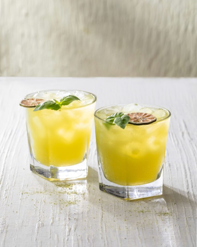 Two glasses hold a Matcha Mule with a lime wheel and sprig of mint on top of the glasses all on a white background.
