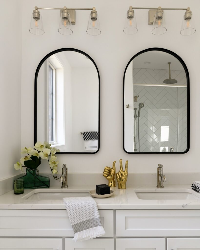Two mirrors in a bathroom with two separate sink parts and gold faucets.