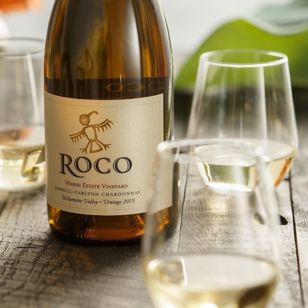 A bottle of ROCO wine for father's day beside two clear glasses of white wine.