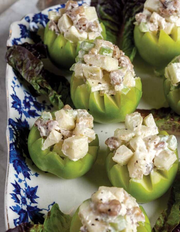 Cut open apples hold a gilded age Waldorf Salad on a blue and white plate.