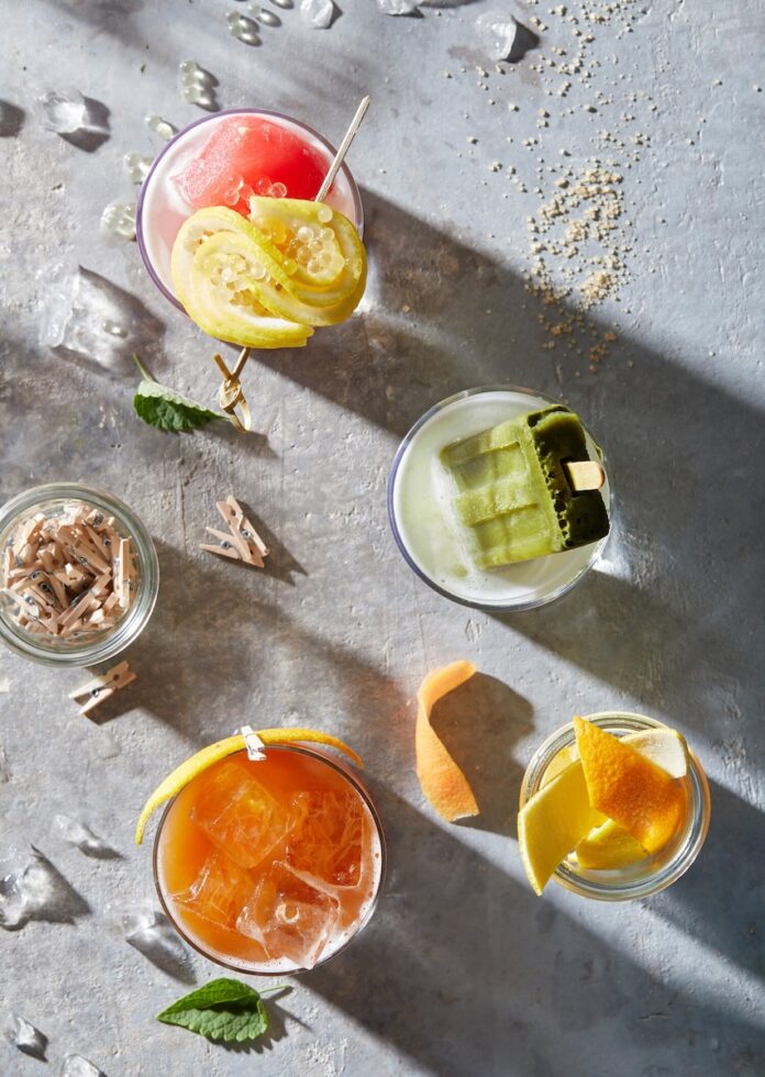 Four different craft mocktail recipes sit on a table with fruit garnishes and little ooden clips around them.
