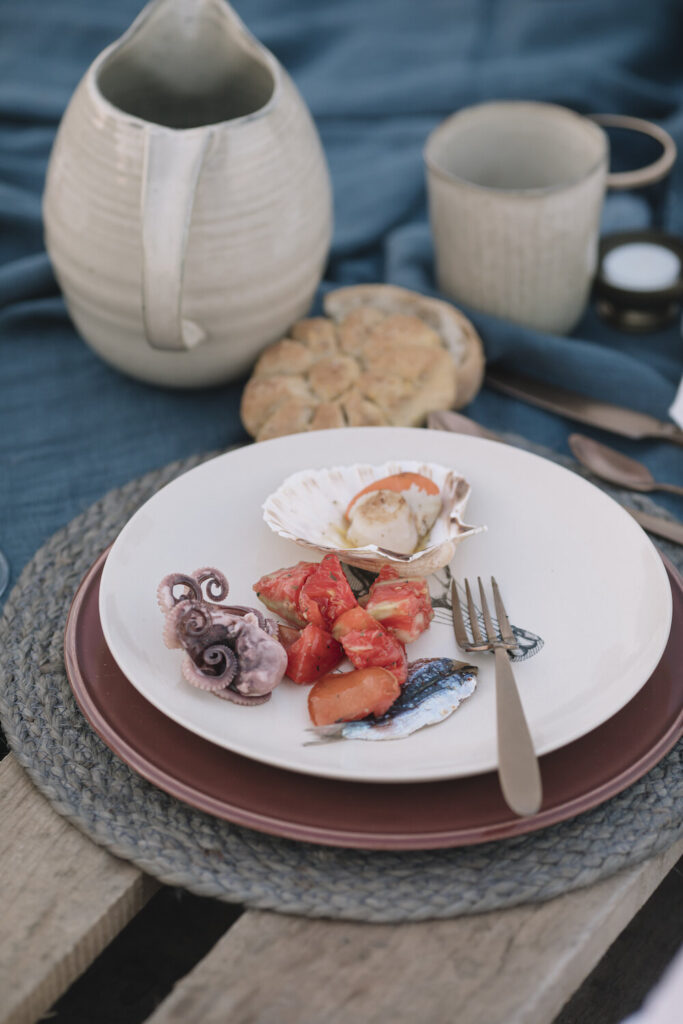 A white plate holds baby octopus, scallops, and sardines as a part of a seafood picnic.