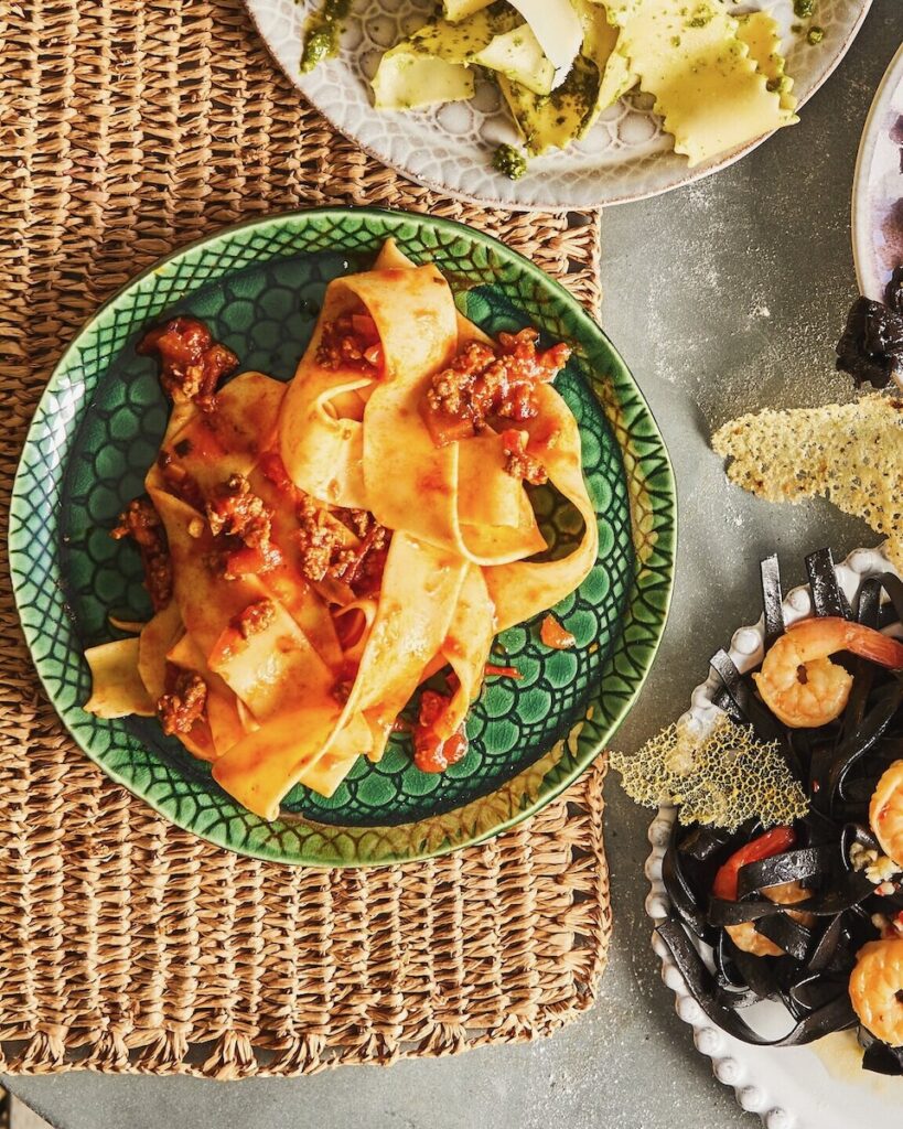 A plate of flat-noodle wide pasta with a meat bolognese ragu sauce on top, all sitting on a green plate.
