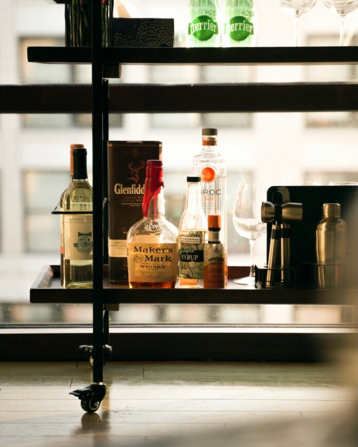 The bottom of a bar cart with various bottles of liquor on the shelf.