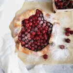 A Cherry Galette sits open faced on a countertop with powdered sugar and cherries everywhere.