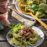 A small plate of Easy Pesto Pasta with basil, sausage, pesto sauce, and asparagus as a large plate of the dish sits in the background.