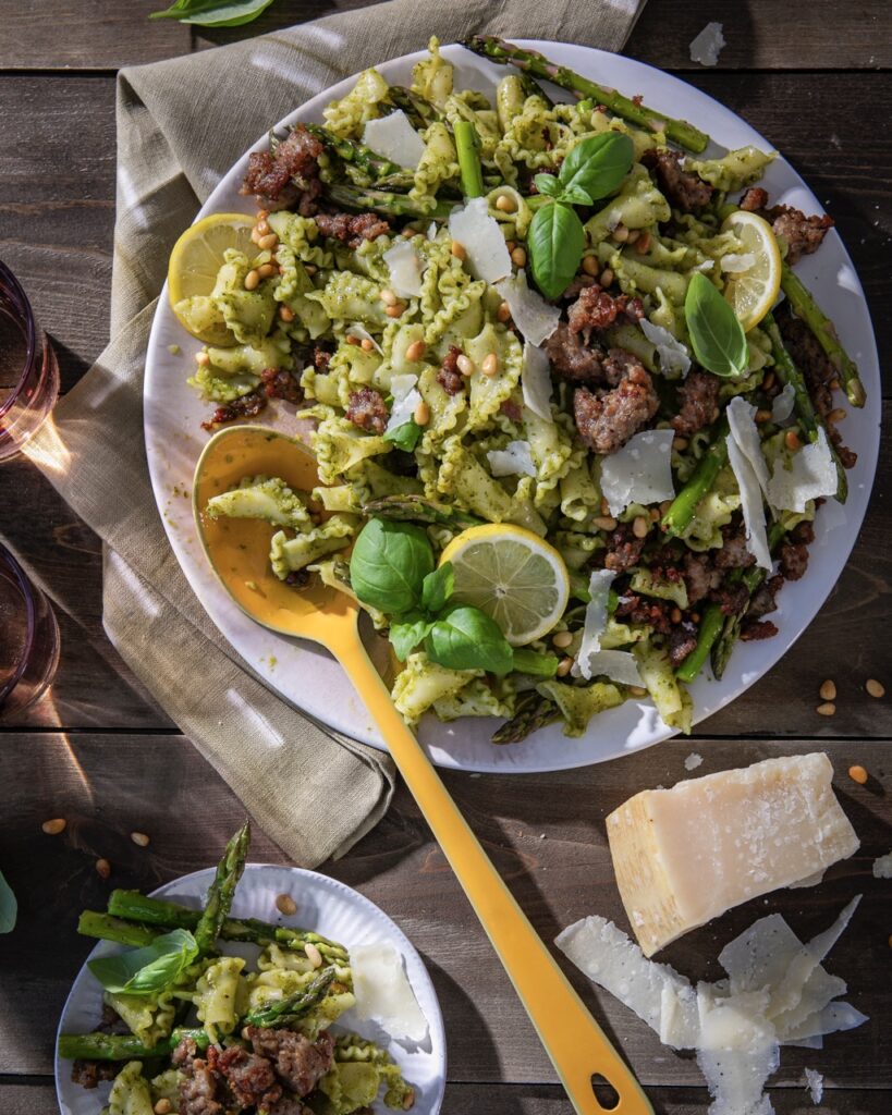 A plate full of Easy Pesto Pasta with sausage, lemon slices, and asparagus all in a green sauce.