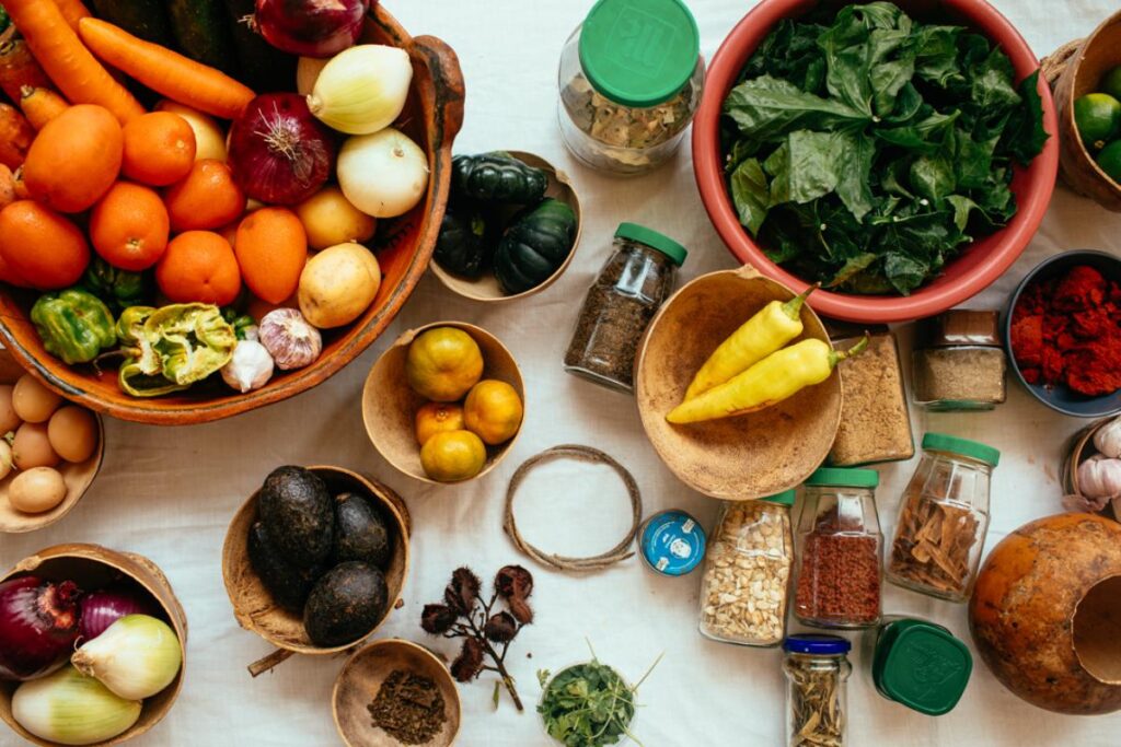 A vibrant assortment of freshly harvested ingredients, including various colorful vegetables, fruits, and spices, are laid out on a white cloth.