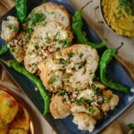 Slices of Gobi Musallam, spiced whole cauliflower, sit on a baking sheet with whole green chiles.