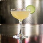 A cocktail glass with a Hemingway Daiquiri featuring a lime wheel garnish on a metal counter.