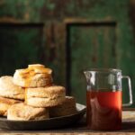 A stack of Hot Honey buttermilk Biscuits sit beside a pitcher of hot honey.
