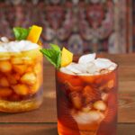 isle of palms cocktail in two glasses with a dark reddish brown tint and a yellow and green garnish
