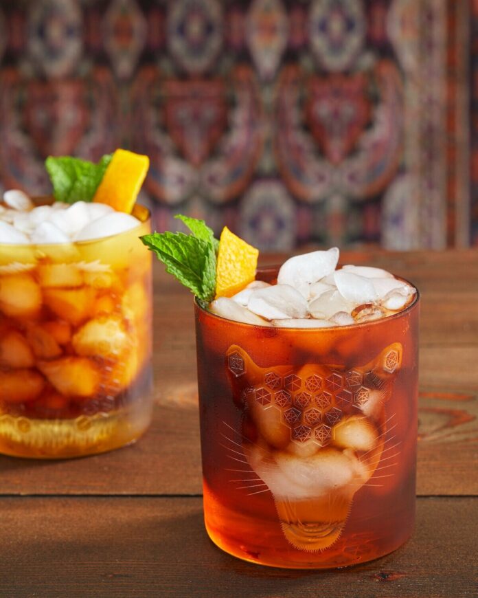isle of palms cocktail in two glasses with a dark reddish brown tint and a yellow and green garnish