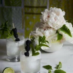 On a table covered in a white tablecloth sits two cocktails, white/clear in color. The Chamomile Lavender Spritz are garnished with flowers.