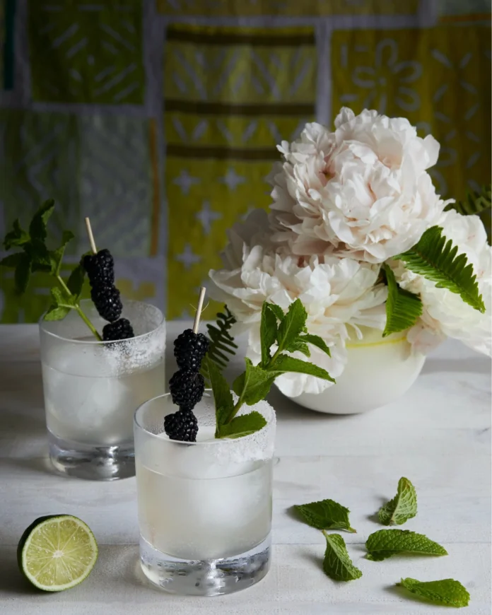 On a table covered in a white tablecloth sits two cocktails, white/clear in color. The Chamomile Lavender Spritz are garnished with flowers.