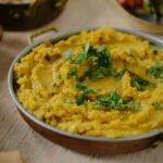 A bowl full of Masoor Dal in a yellow color with an herb garnish on top.