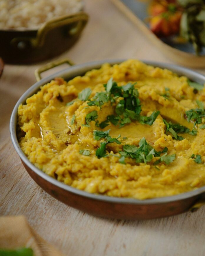 A bowl full of Masoor Dal in a yellow color with an herb garnish on top.