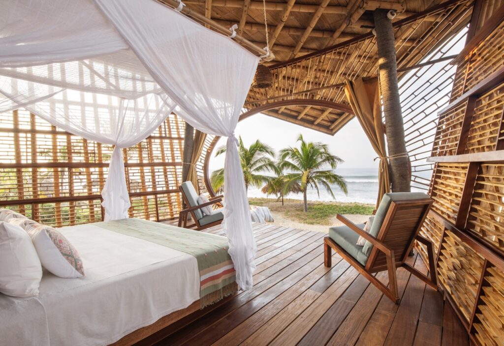A white bed and lounge chair sit in a hut at Playa Viva looking out to the palm trees.