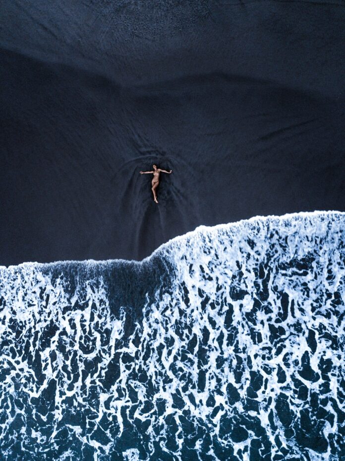 A naked woman laying in the dark blue ocean as the waves come in.