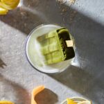 A glass holds a green mocktail with a matcha latte popsicle in it.