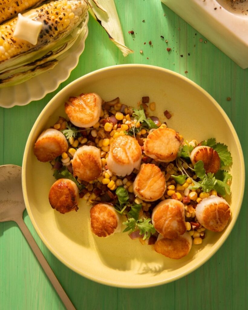 Seared Scallops with Warm Corn & Chorizo Salsa on a yellow dish with green background.