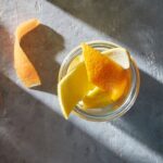 A mocktail holds a mason jar glass with various orange peels.