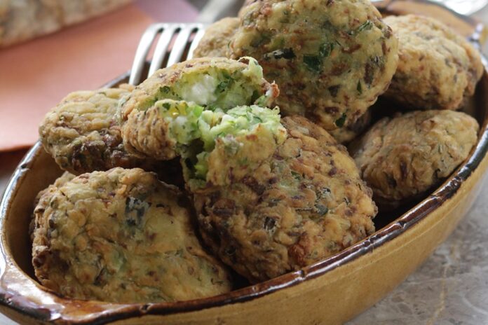 A bowl full of zucchini fritters sits on a table with a fork in the background.