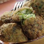 A bowl full of zucchini fritters sits on a table with a fork in the background.