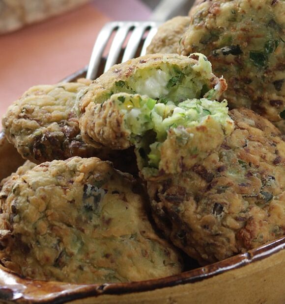 A bowl full of zucchini fritters sits on a table with a fork in the background.