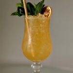Yellow-organge rum punch with green garnish and straw