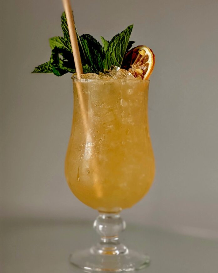 Yellow-organge rum punch with green garnish and straw