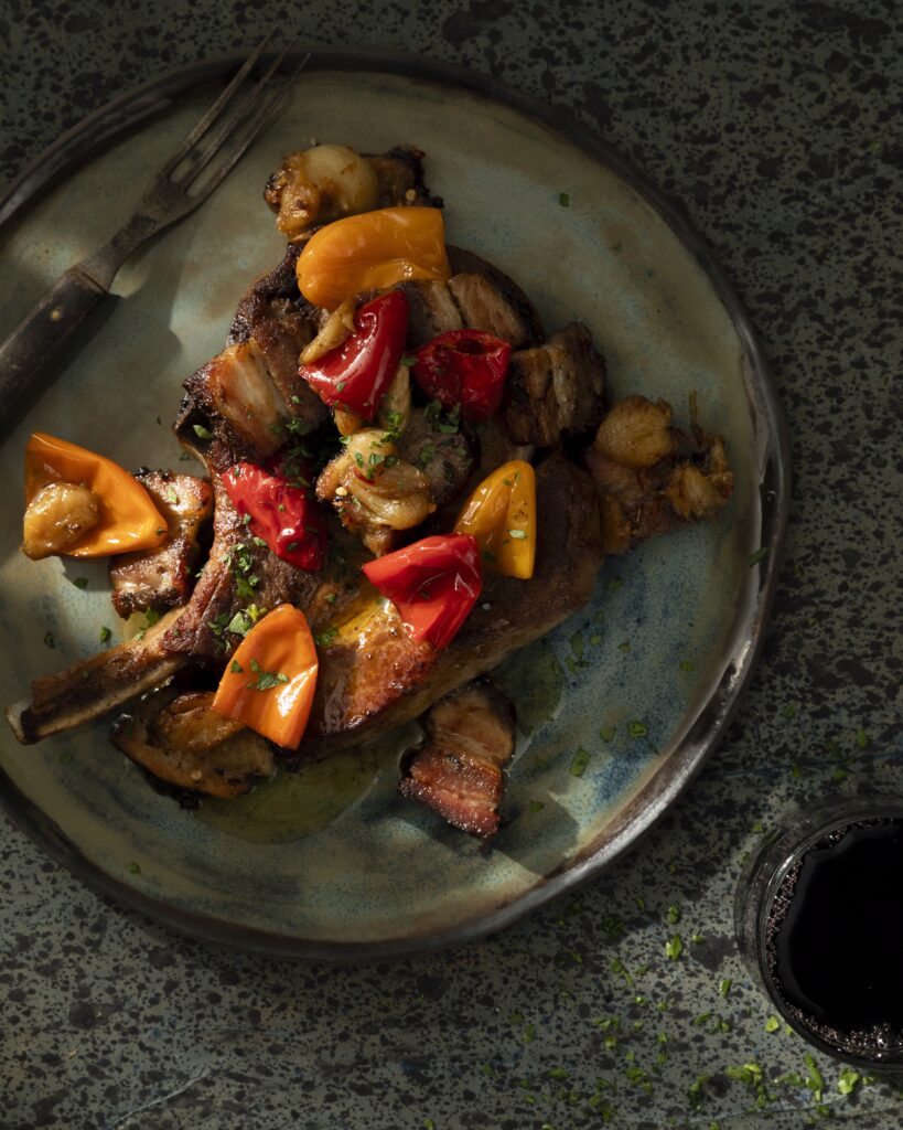 An aerial shot of a gray/blue/green plate holding a Pork Chop with Bacon and Pickled Peppers