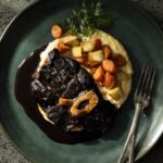 An above shot of a green plate with high edges, holding Beef Shank with Confit Garlic and Polenta