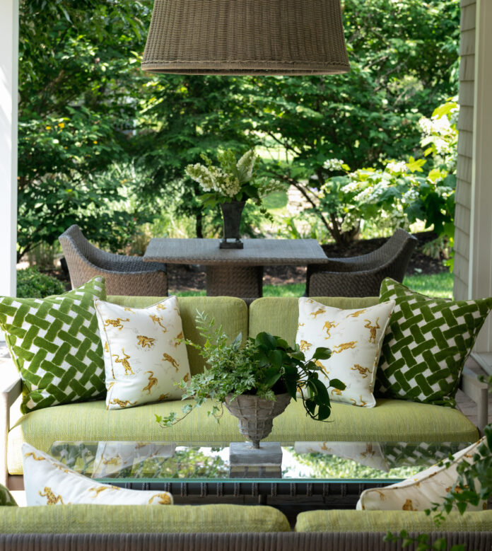 A green sofa sits with green pattern pillows below a lamp shade chandelier.