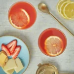 An above shot of two Aperol sour cocktails, light red in color, garnished by lemon slices.