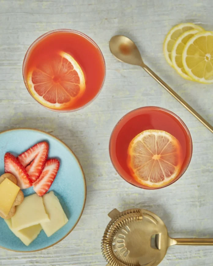 An above shot of two Aperol sour cocktails, light red in color, garnished by lemon slices.