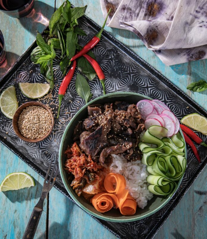 A board holds a beef bulgogi bowl and then cilantro, red peppers, and lime slices.