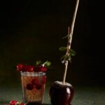 A Bourbon Apple Smash cocktail in a glass, next to a caramel-dipped apple.