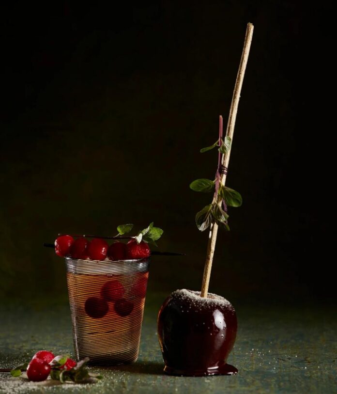 A Bourbon Apple Smash cocktail in a glass, next to a caramel-dipped apple.
