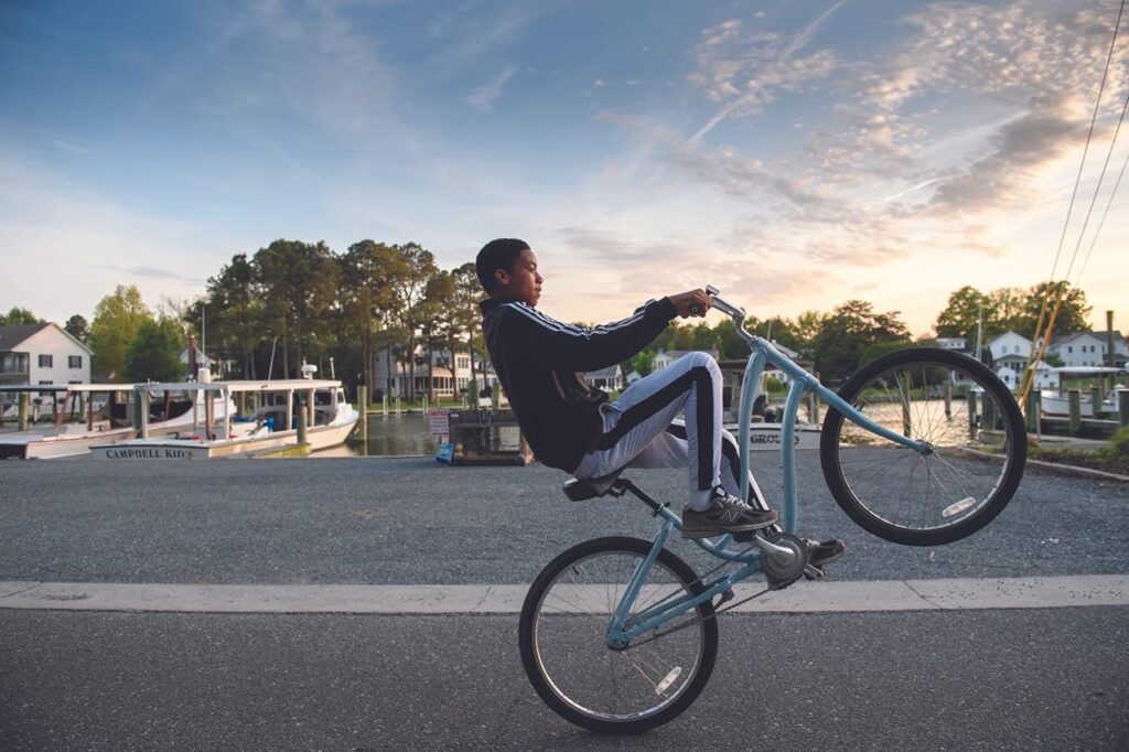 A kid pops a wheely on his bike going down the road.
